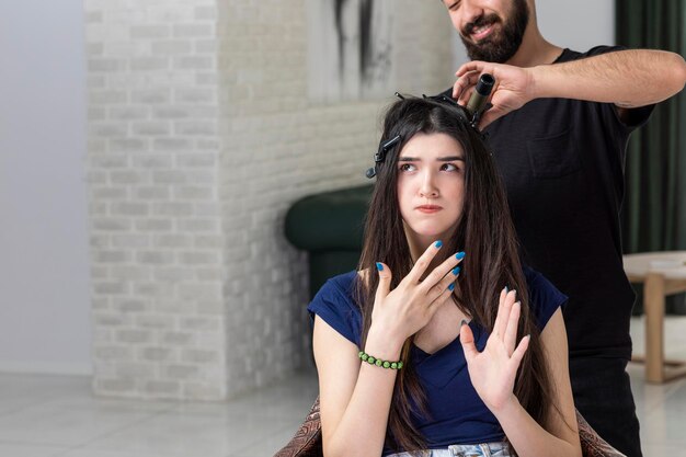 Una joven seria sentada en la silla mientras el peluquero se peina Foto de alta calidad