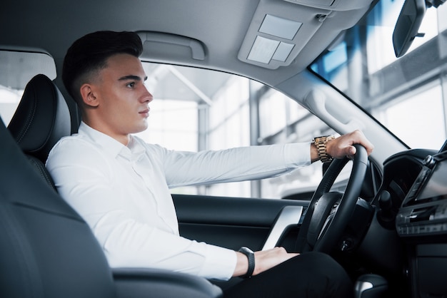 Un joven se sienta en un automóvil recién comprado al volante, una compra exitosa.