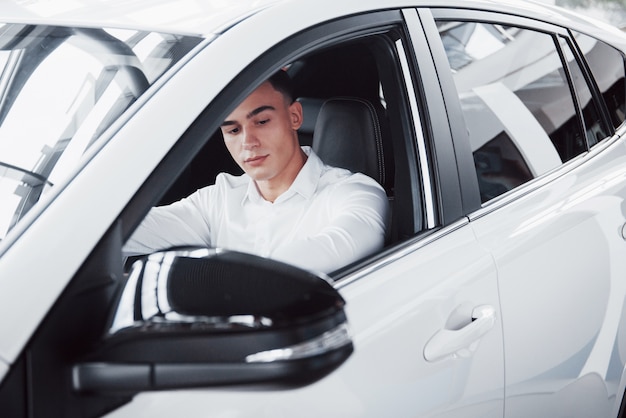 Un joven se sienta en un automóvil recién comprado al volante, una compra exitosa.