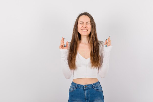 La joven se siente feliz cruzando los dedos sobre fondo blanco.