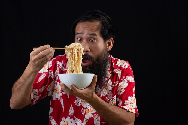 El joven se siente sorprendido con lo deliciosos que son los fideos instantáneos. Joven es disfrutar eatting fideos instantáneos en casa.