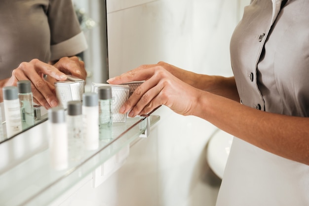 Joven sirvienta del hotel poniendo accesorios de baño en un baño