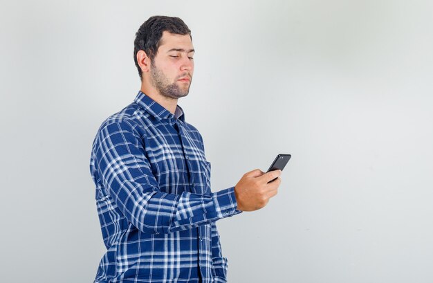 joven con smartphone en camisa a cuadros y mirando con cuidado.