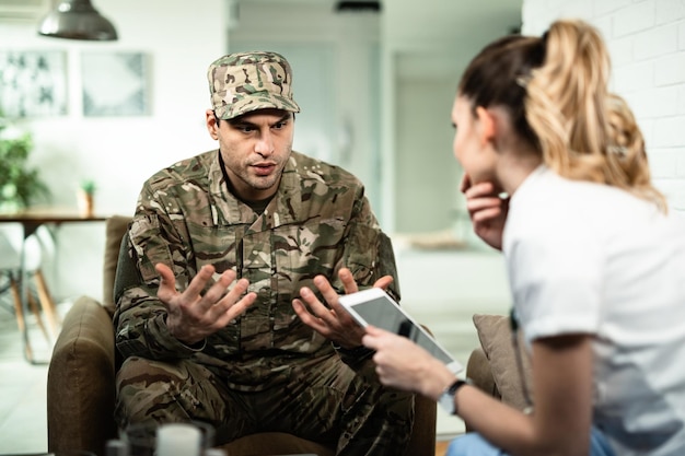 Joven soldado angustiado gesticulando mientras habla con un trabajador de la salud que lo visita en casa