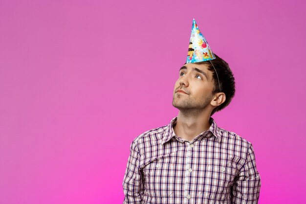 Joven con sombrero de cumpleaños sobre pared púrpura. Fiesta de cumpleaños.