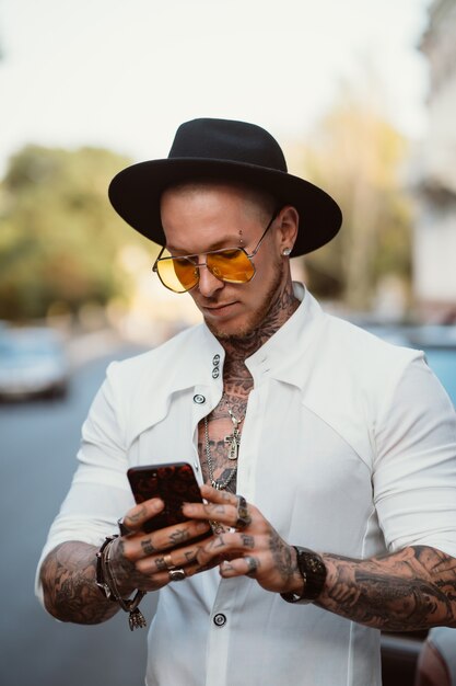 Un joven con sombrero y gafas de sol sostiene un teléfono móvil en sus manos