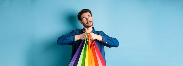 Joven soñador sosteniendo coloridas bolsas de compras e imaginando algo mirando la esquina superior izquierda e