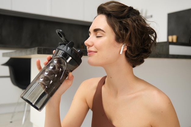 Foto gratuita una joven sonriente y activa con ropa deportiva se sienta en una estera de yoga con una botella de agua y se mantiene hidratado.