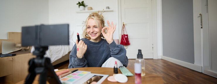 Foto gratuito una joven sonriente y alegre grabando un vlog mostrando un gesto de "okay ok" y su lápiz labial favorito