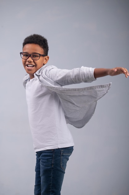 Un joven sonriente y alegre de piel oscura con elegantes gafas preparándose para saltar ante la cámara