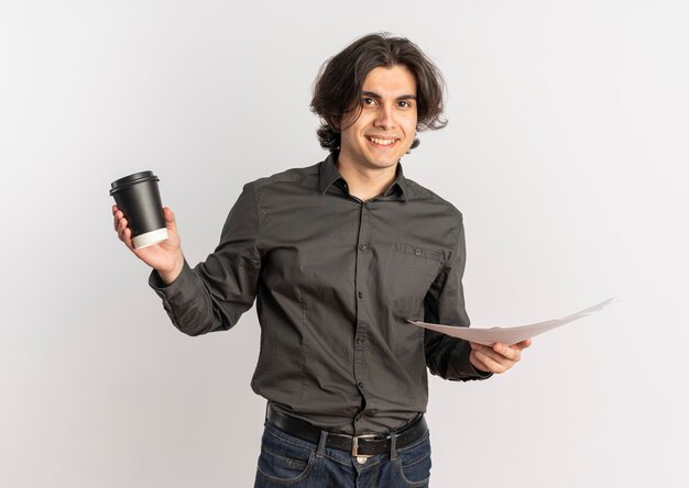 Joven sonriente apuesto hombre caucásico sostiene una taza de café y hojas de papel blanco en blanco aisladas sobre fondo blanco con espacio de copia
