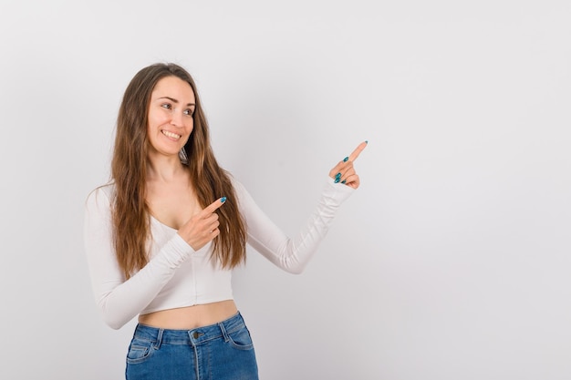 Una joven sonriente apunta hacia arriba con los dedos índices sobre fondo blanco.