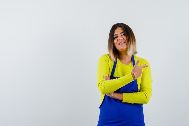 La joven sonriente apunta a la derecha con el dedo índice sobre fondo blanco.