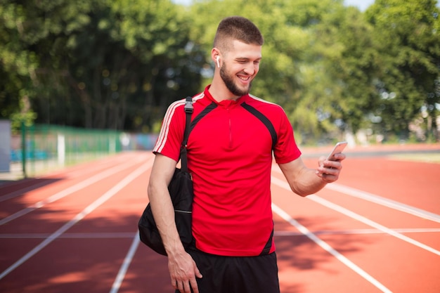 Foto gratuita joven sonriente con auriculares inalámbricos felizmente usando el celular mientras pasa tiempo en el estadio