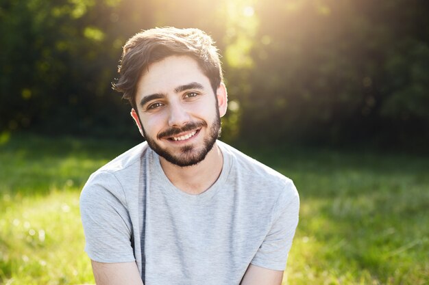 Joven sonriente con cabello oscuro, cejas gruesas, ojos atractivos y barba con camiseta casual sentado en Groenlandia