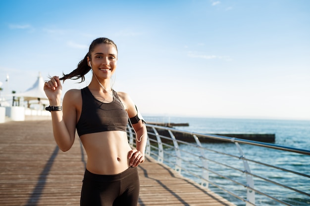 Joven sonriente chica fitness lista para ejercicios deportivos junto al mar