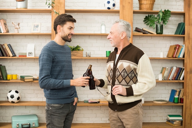 Joven sonriente chico clanging botellas con hombre de edad