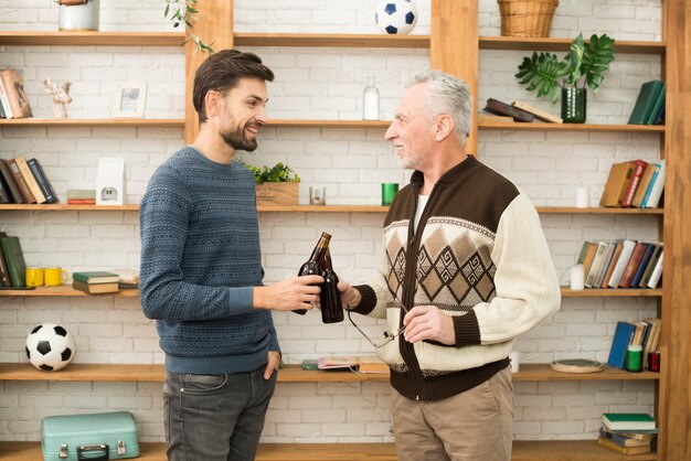 Joven sonriente chico clanging botellas con hombre de edad