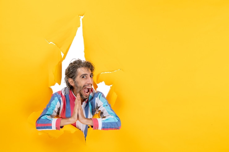 Foto gratuito joven sonriente y emocional posa en fondo de agujero de papel amarillo rasgado haciendo gesto de agradecimiento