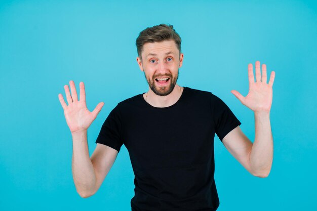 El joven sonriente está levantando las manos sobre fondo azul.