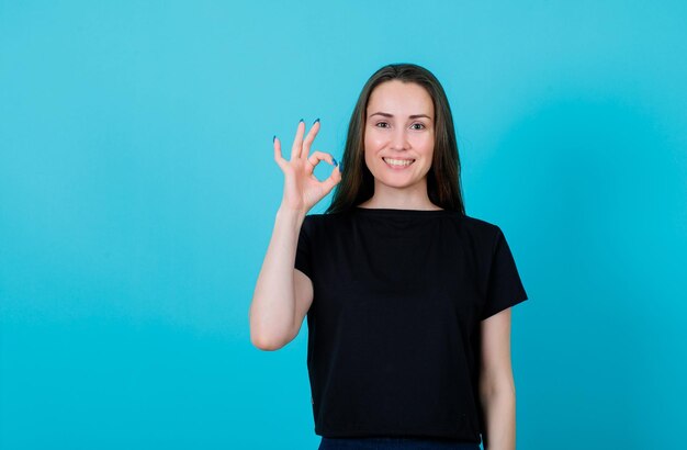 Una joven sonriente está mostrando un gesto correcto en el fondo azul