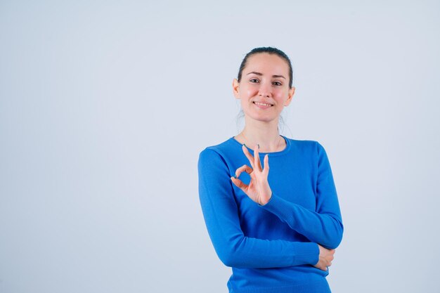 Una joven sonriente está mostrando un gesto correcto en el fondo blanco