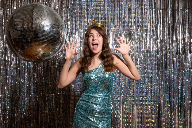 Joven sonriente feliz encantadora dama con vestido azul verde brillante con lentejuelas con corona y apuntando hacia arriba en la fiesta