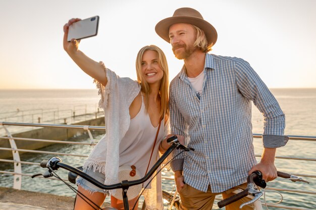 Joven sonriente feliz hombre y mujer viajando en bicicleta tomando selfie foto en la cámara del teléfono