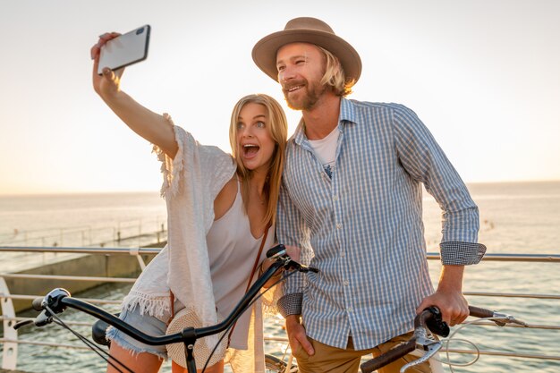 Joven sonriente feliz hombre y mujer viajando en bicicleta tomando selfie foto en la cámara del teléfono