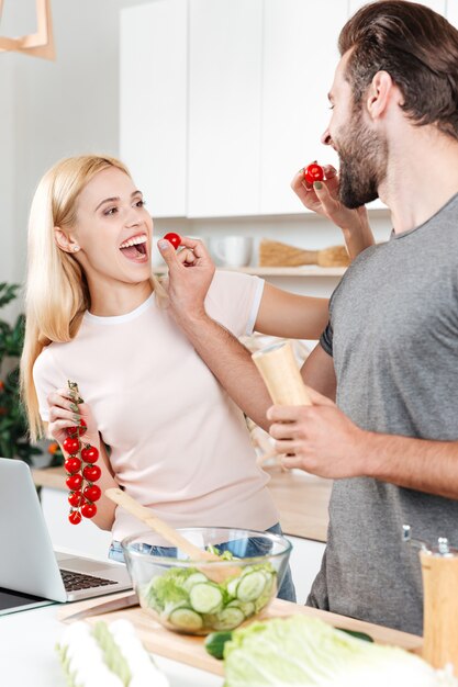 Joven sonriente hombre y mujer en la cocina cocinando con laptop