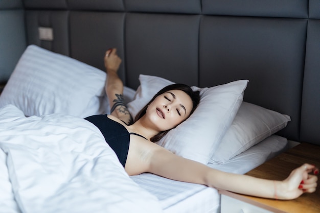 Joven sonriente mujer acostada en la cama y estirar los brazos