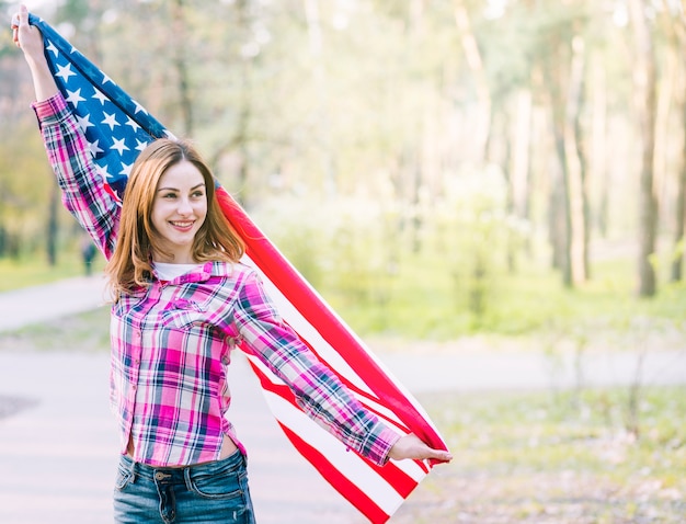 Foto gratuita joven sonriente mujer agitando bandera estadounidense en el parque