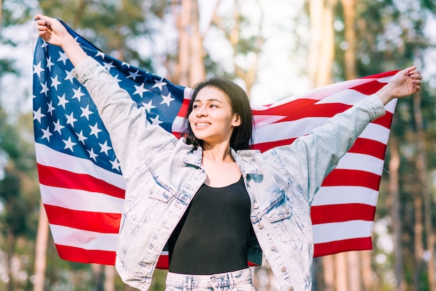 Joven sonriente mujer sosteniendo la bandera de Estados Unidos el cuatro de julio
