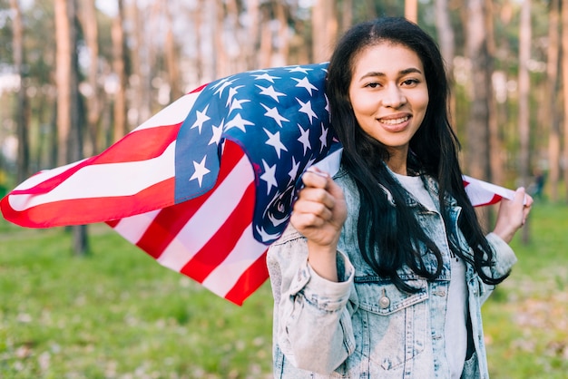Joven sonriente mujer sosteniendo la bandera de Estados Unidos volando