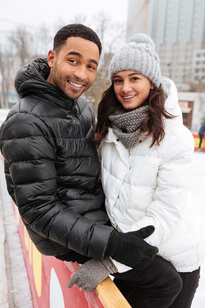 Joven sonriente pareja amorosa patinando en la pista de hielo al aire libre.