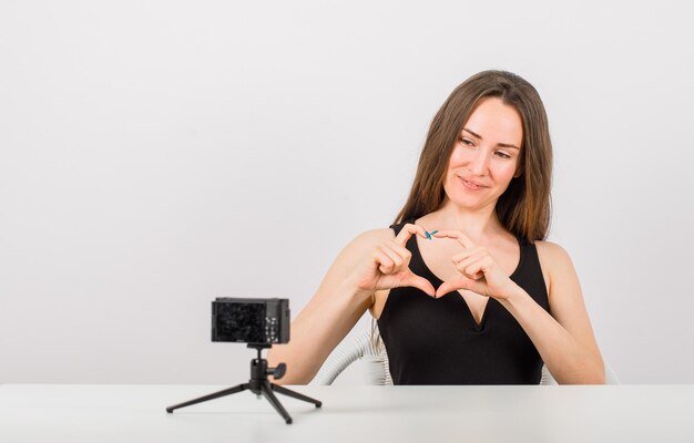 Una joven sonriente posa ante la cámara mostrando un gesto de corazón en el fondo blanco