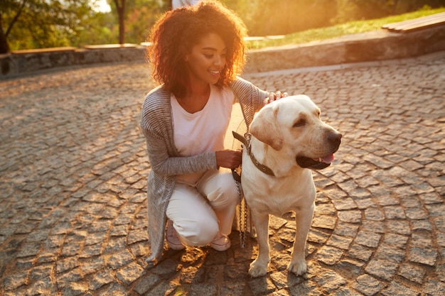 Joven sonriente en ropa casual sentado y abrazando a perro en el parque