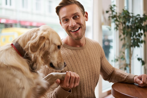 Foto gratuita un joven sonriente sostiene su pata de perro en la mano y parece feliz concepto de café apto para mascotas y