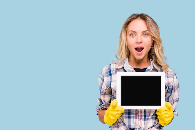 Foto gratuita joven sorprendida con la boca abierta con tableta digital de pantalla en blanco sobre fondo azul