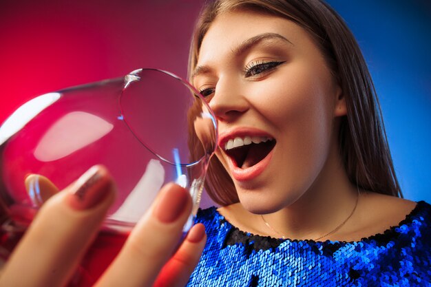 La joven sorprendida en ropa de fiesta posando con una copa de vino.