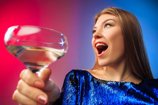 La joven sorprendida en ropa de fiesta posando con una copa de vino.