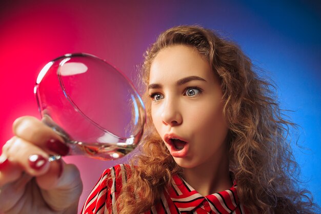 La joven sorprendida en ropa de fiesta posando con copa de vino.