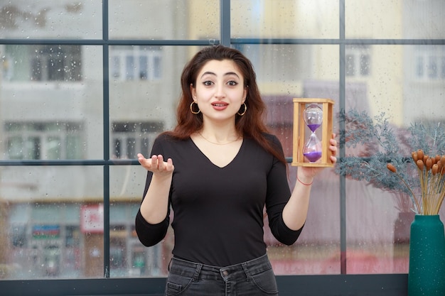 Una joven sorprendida sosteniendo un reloj de arena y mirando a la cámara Foto de alta calidad