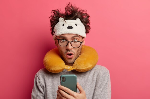 Joven sorprendido con cabello desordenado mira fijamente smartphone