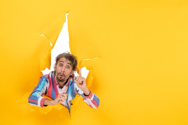 Foto gratuito joven sorprendido posa en el fondo del agujero de papel amarillo rasgado