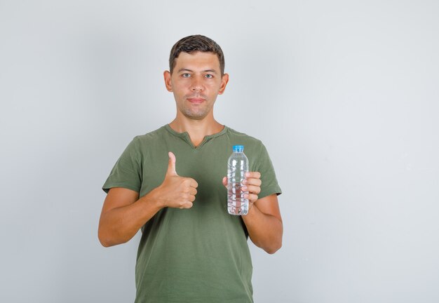 Joven sosteniendo una botella de agua y mostrando el pulgar hacia arriba en la vista frontal de la camiseta verde militar.