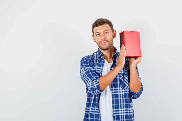 Joven sosteniendo la caja actual y sonriendo en camisa, vista frontal.