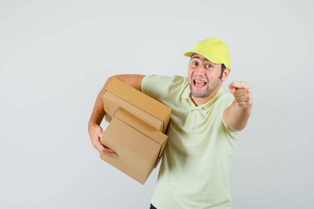 Foto gratuita joven sosteniendo cajas de cartón apuntando a la cámara con gorra de camiseta y mirando alegre