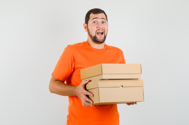 Joven sosteniendo cajas de cartón en la vista frontal de la camiseta naranja.