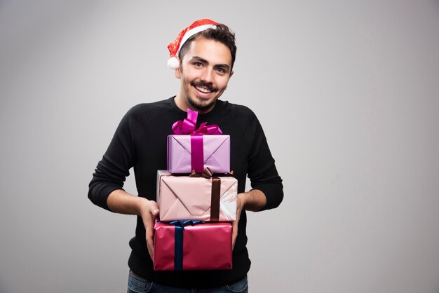 Un joven sosteniendo cajas de regalo sobre una pared gris.